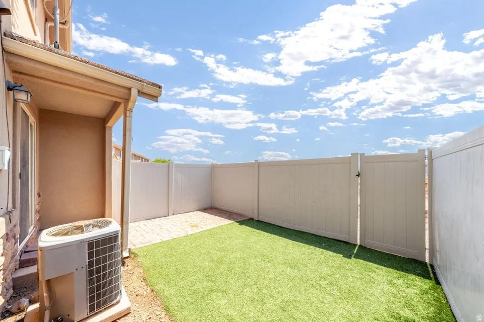 Private fenced yard with artificial turf and a paved patio area