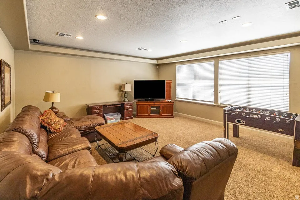 Recessed lighting, tray ceiling, two windows with blinds, built-in entertainment console, and wall-to-wall carpeting