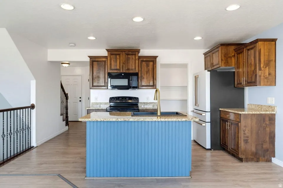 Kitchen featuring a blue-paneled island with an undermount sink, recessed lighting, wood-finish flooring, and wood cabinetry with granite countertops