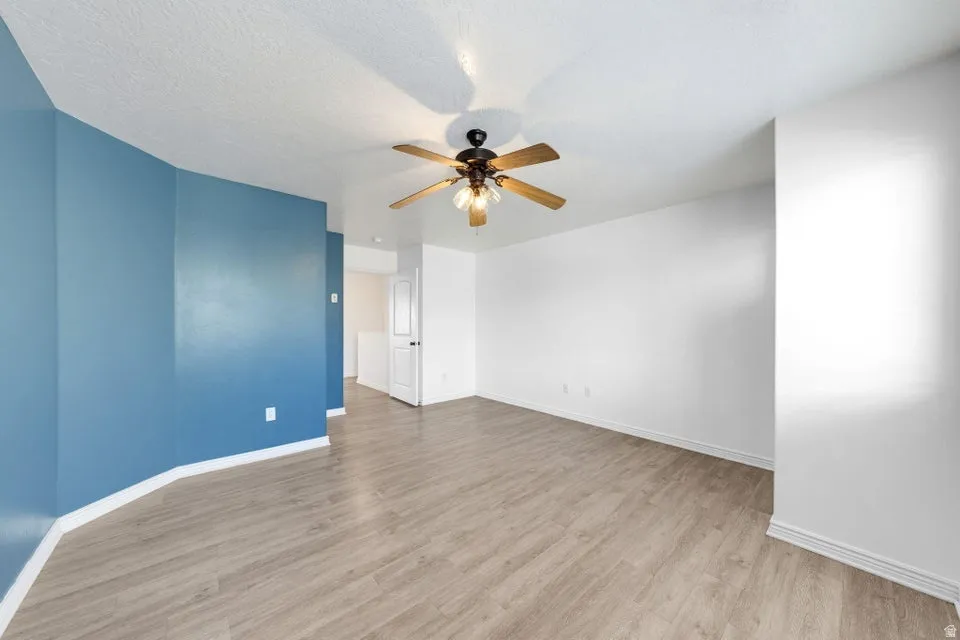 Spacious room featuring wood-finish flooring, a ceiling fan with light fixture, and a mix of accent and neutral walls