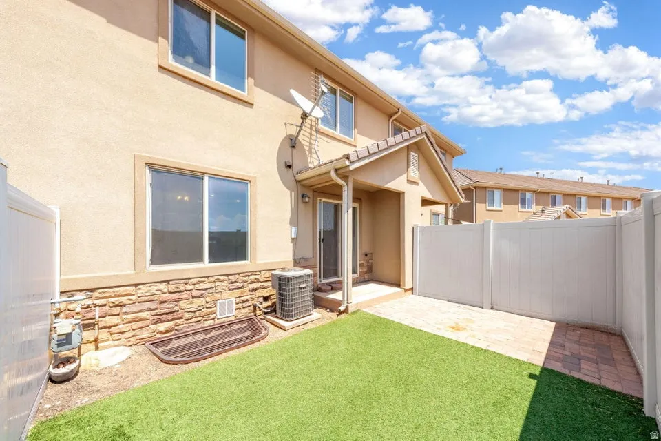Enclosed outdoor space featuring artificial turf, a paver patio, and a privacy fence