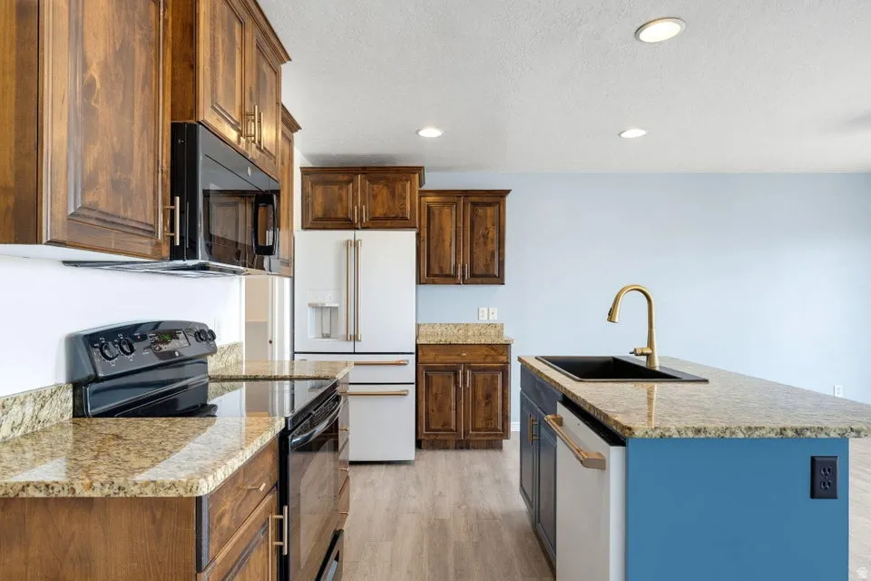 Kitchen featuring wood cabinetry, light-toned granite countertops, a black electric range, a white refrigerator, and a kitchen island with a black sink and brass faucet