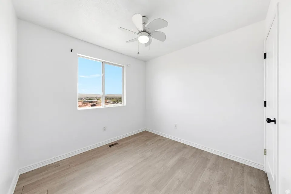 White walls, wood-finish flooring, and a ceiling fan with integrated lighting