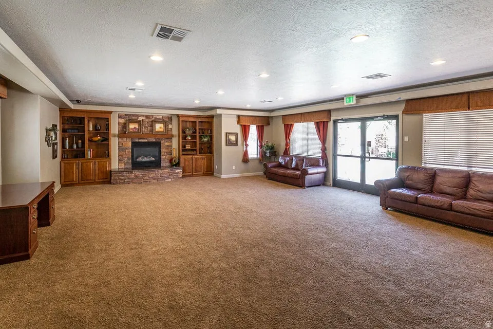 Spacious living area featuring a stone fireplace, built-in shelving, recessed lighting, and expansive carpeted flooring