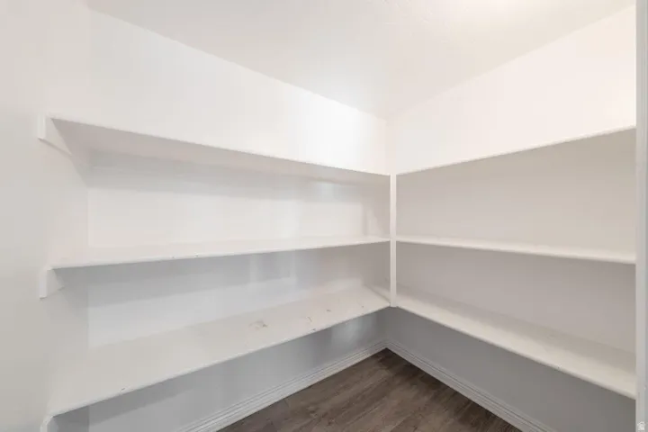Walk-in pantry featuring extensive white shelving and wood-finish flooring