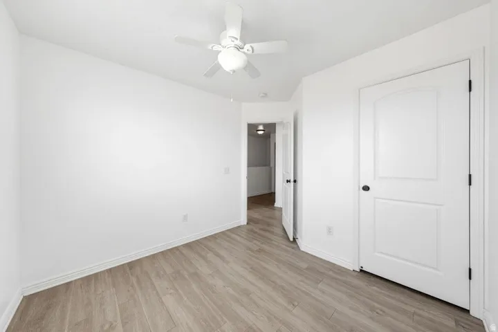 Wood-finish flooring, white walls, ceiling fan, and white paneled doors