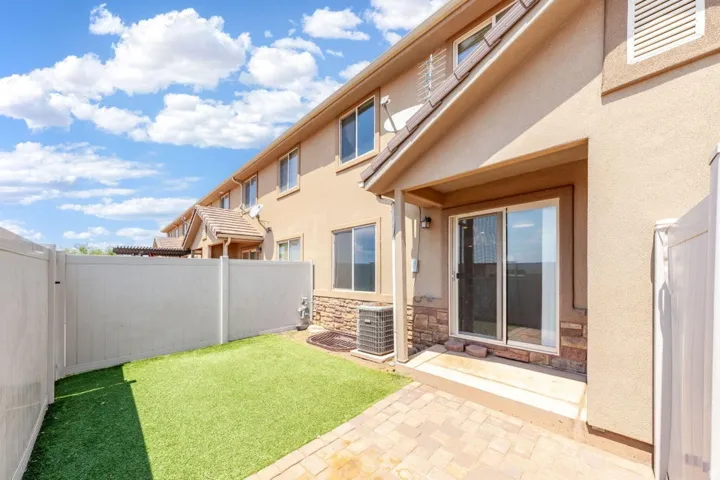 Private fenced patio featuring artificial turf and paver stones
