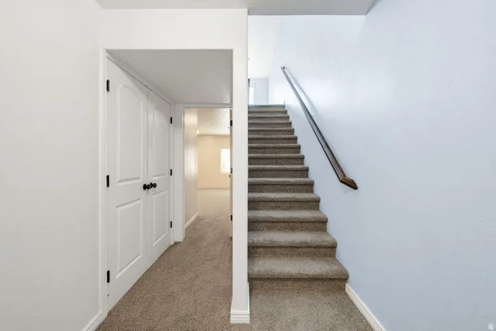 Bright staircase with carpeted treads and metal handrail, opening to a hallway featuring neutral carpeting and clean white walls