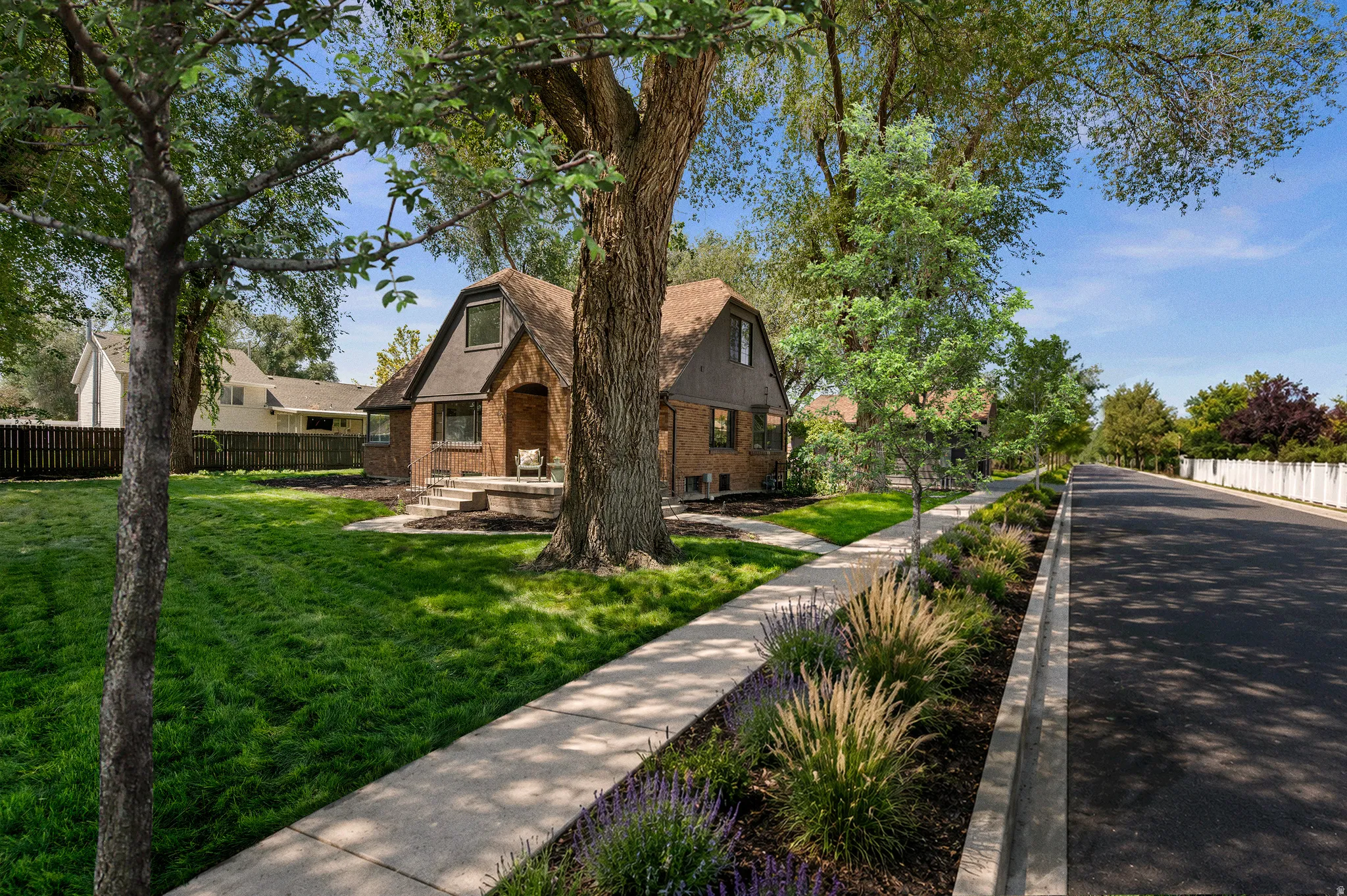 Brick exterior with dormer windows, front porch, mature trees, and a manicured lawn
