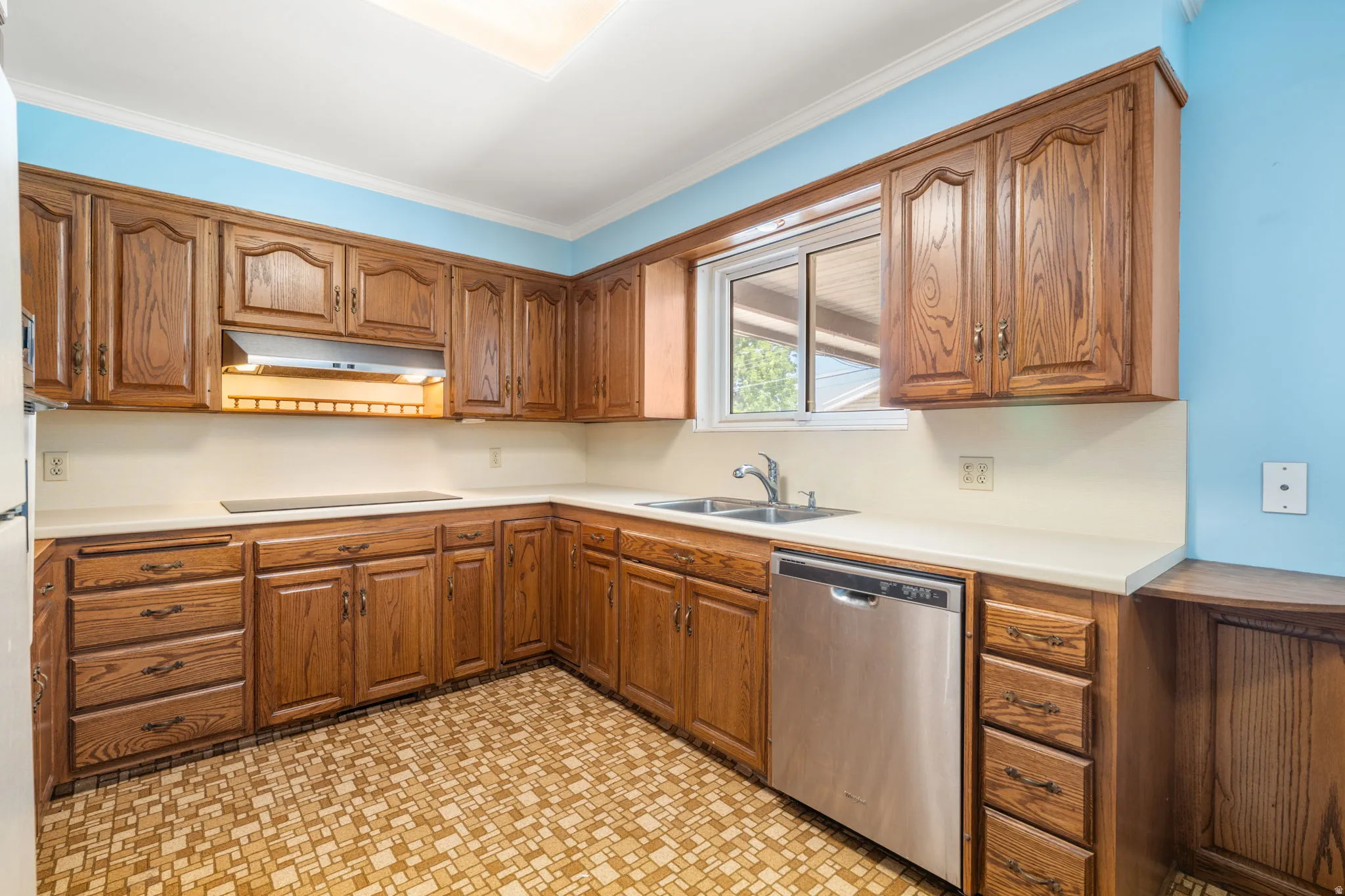 Kitchen featuring wood cabinetry, white countertops, a stainless steel dishwasher, and a double basin sink