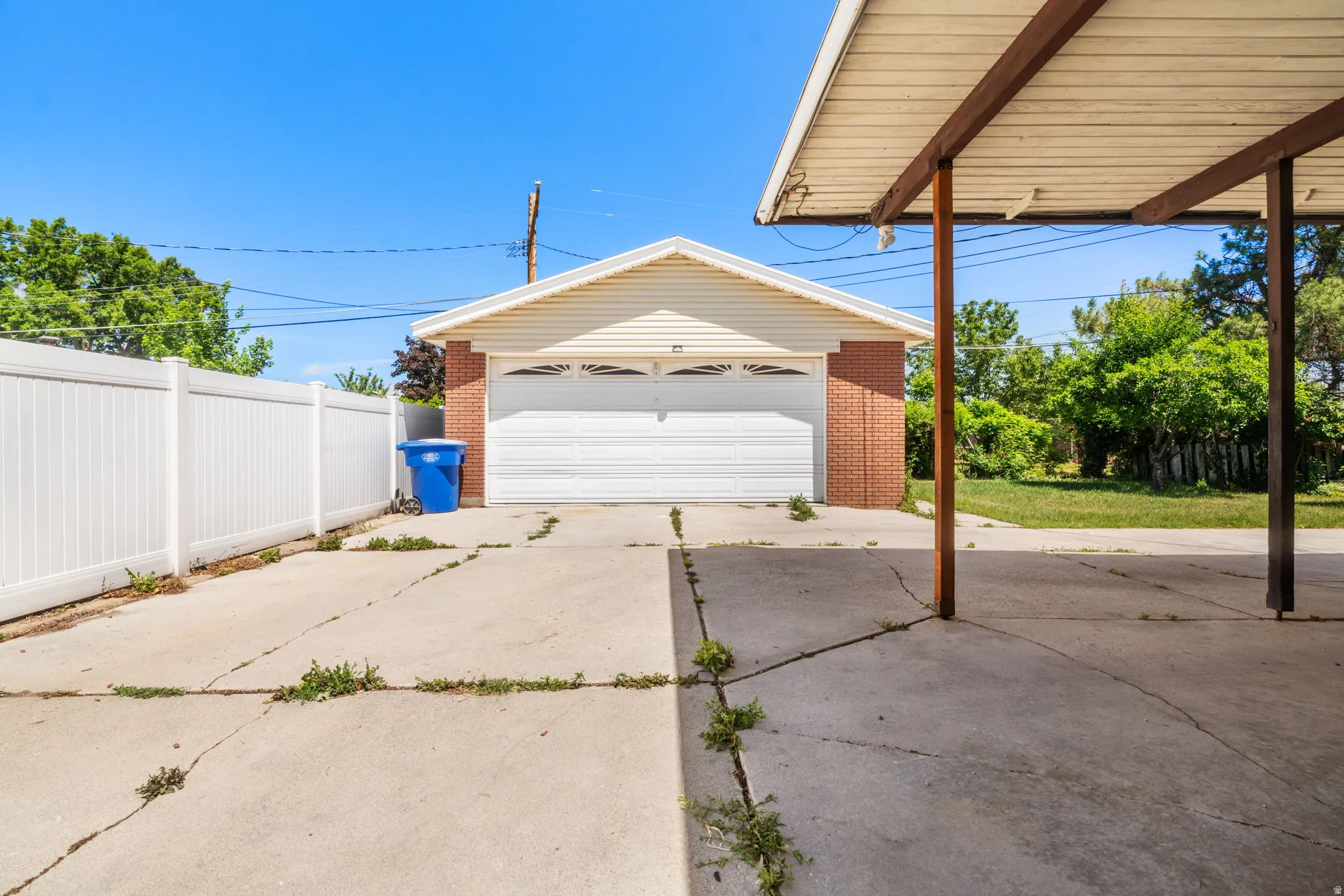 Detached garage with brick and siding exterior, white garage door, and a covered carport structure