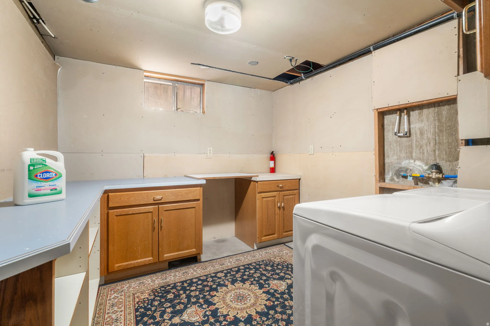 Functional utility space featuring wood-finish cabinetry, light-toned countertops, and exposed ceiling infrastructure