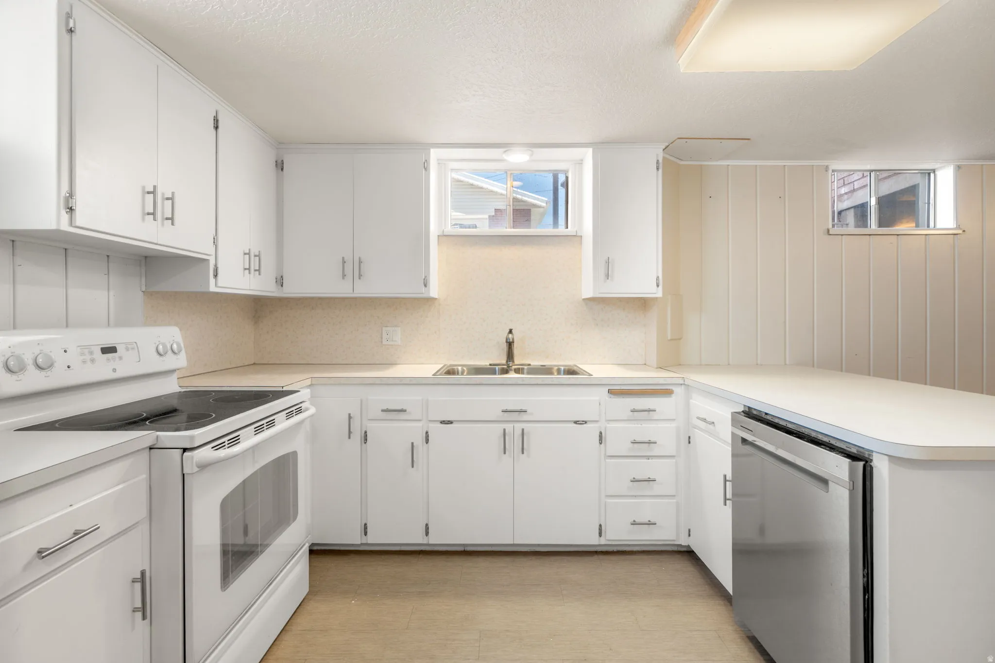 White cabinetry with brushed nickel hardware, solid surface countertops, stainless steel dishwasher, white electric range, and light wood-finish flooring
