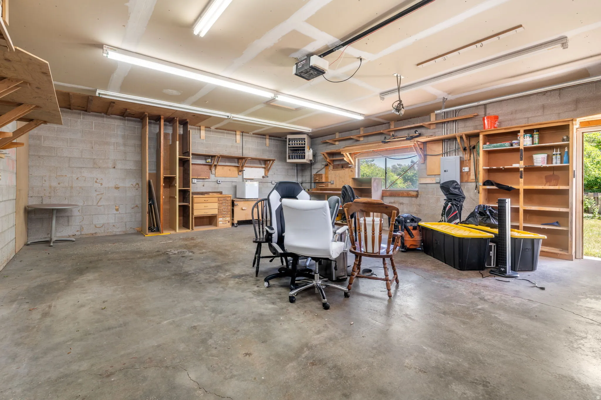Concrete flooring, exposed concrete block walls, built-in shelving, overhead lighting, and an overhead garage door opener