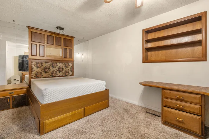 Built-in wooden shelving unit, carpeted flooring, and a wall-mounted wooden desk