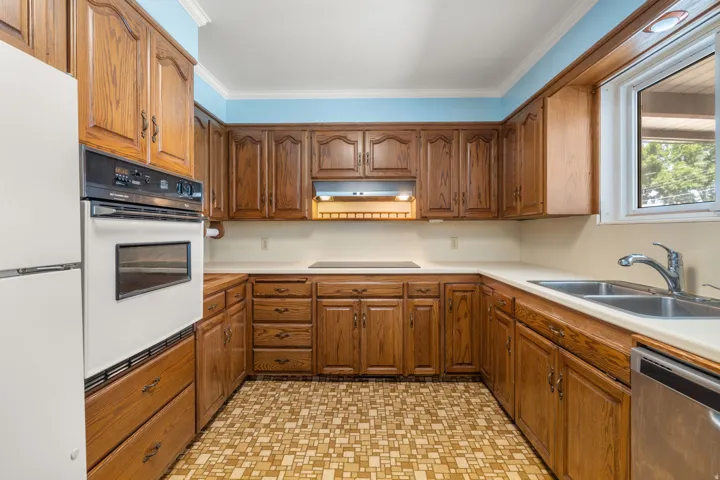 Kitchen featuring wood cabinetry, solid surface countertops, dual basin stainless steel sink, and a built-in wall oven