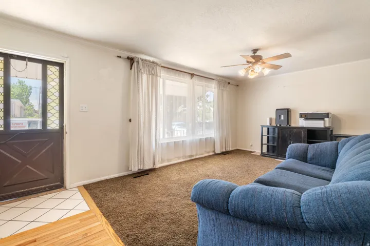 Spacious living area featuring a ceiling fan with integrated lighting, multiple windows, and a built-in media console