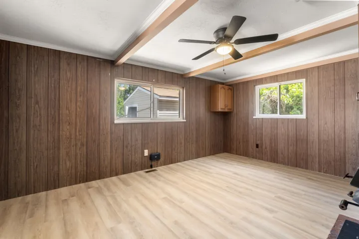 Wood-finish wall paneling, light wood-finish flooring, two windows, and a ceiling fan with integrated lighting