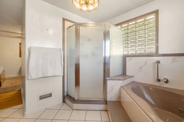 Corner shower enclosure with clear glass block window, accompanied by a built-in tub with a tiled surround