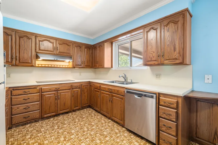 Kitchen featuring wood cabinetry, white countertops, a stainless steel dishwasher, and a double basin sink