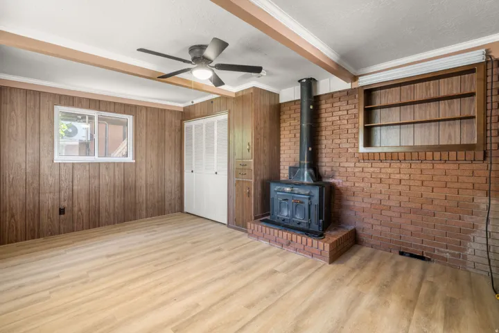 Wood-finish flooring, exposed ceiling beams, wood-paneled walls, brick accent wall with built-in shelving, and a cast iron wood-burning stove