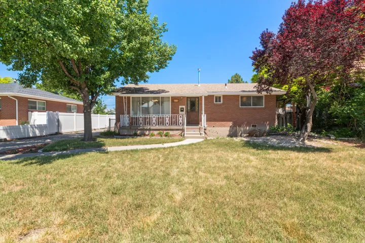 Brick exterior featuring a covered entry, front porch with decorative railing, and mature trees