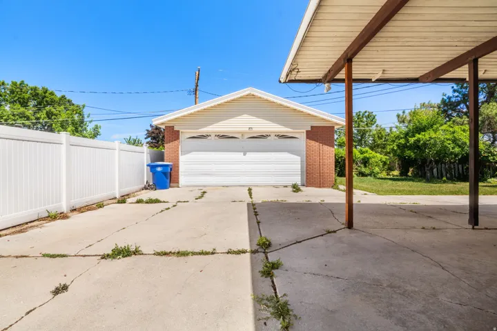 Detached garage with brick and siding exterior, white garage door, and a covered carport structure