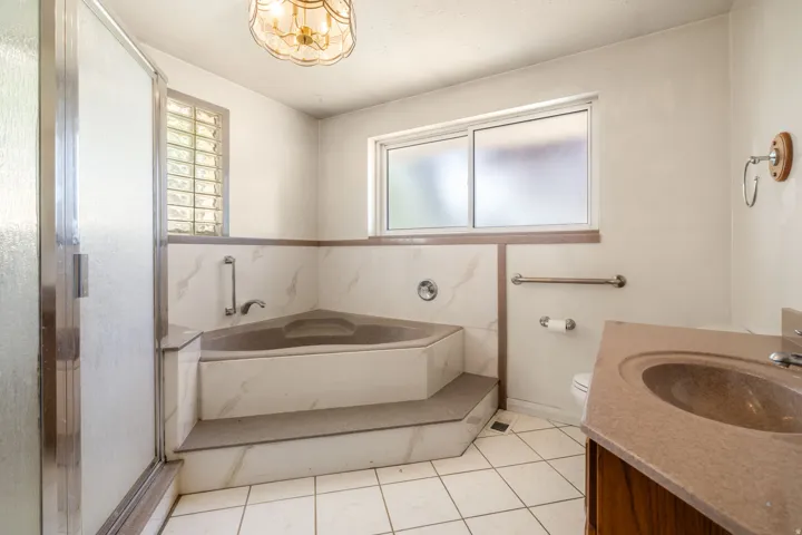 Bathroom featuring a corner bathtub, white tile flooring, a glass-enclosed shower, a frosted window, and a single vanity with an integrated sink