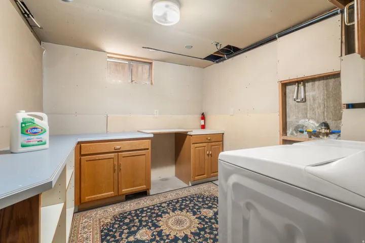 Functional utility space featuring wood-finish cabinetry, light-toned countertops, and exposed ceiling infrastructure