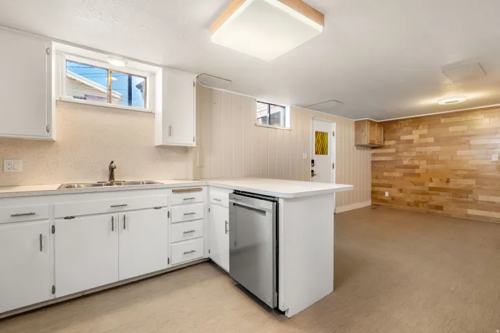 White cabinetry, stainless steel dishwasher, dual basin sink, light-colored backsplash, and wood plank accent wall