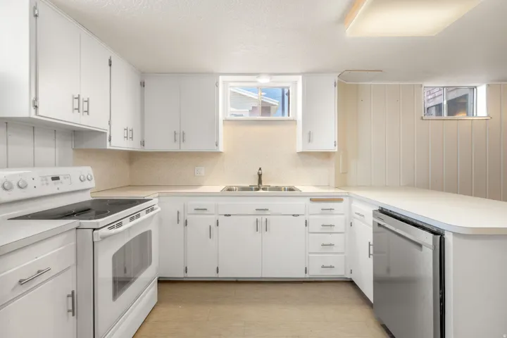 White cabinetry with brushed nickel hardware, solid surface countertops, stainless steel dishwasher, white electric range, and light wood-finish flooring