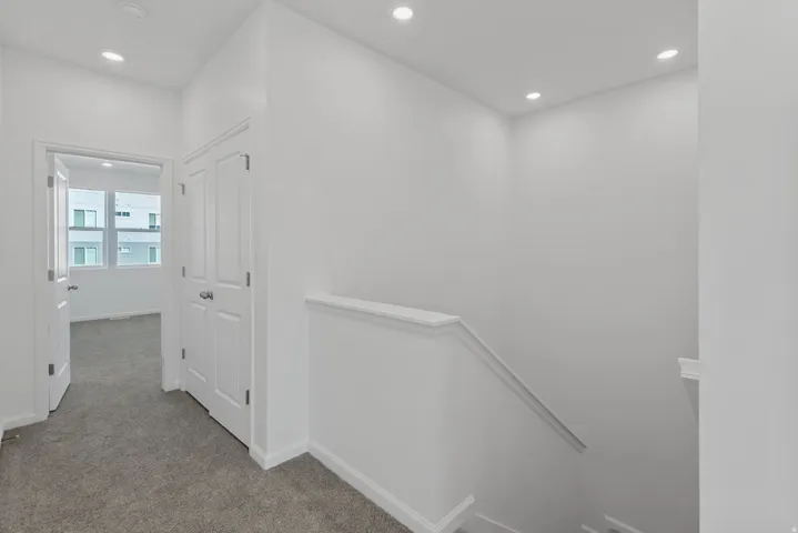 Recessed ceiling lighting, white walls, white trim, carpeted flooring, and a white interior door