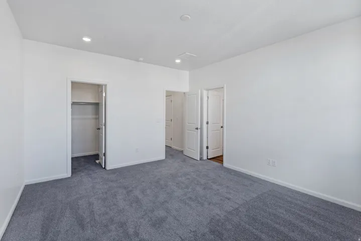 Spacious primary bedroom featuring neutral wall finishes, recessed ceiling lighting, and direct access to a walk-in closet