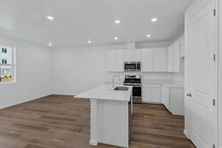 Kitchen island with an undermount sink, stainless steel appliances, white cabinetry, and wood-finish flooring
