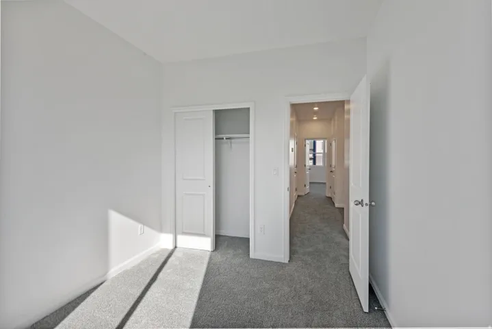Neutral wall paint, gray carpeting, sliding closet doors, and recessed lighting in the hallway