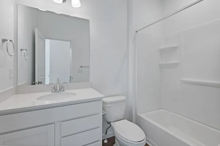 White vanity with a built-in sink and chrome faucet, large mirror, and a white tub/shower combination