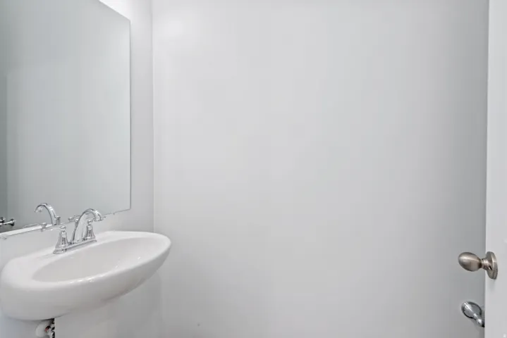 Pedestal sink with chrome faucet, wall-mounted mirror, and neutral wall finish