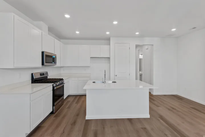 Kitchen featuring white cabinetry, stainless steel appliances, a center island with sink, white countertops, and wood-finish flooring