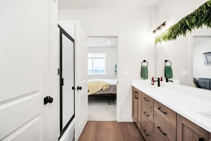 Double vanity with a white countertop and wood-finish cabinetry featuring matte black hardware, paired with wood-finish flooring