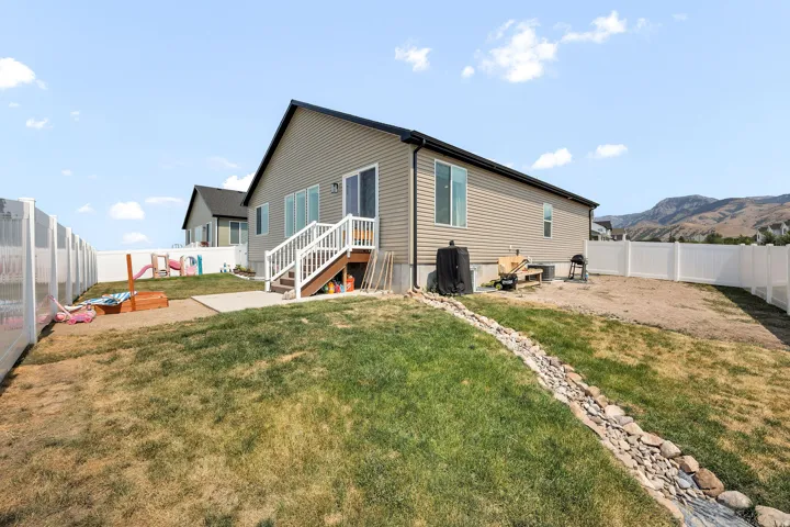 Exterior featuring beige horizontal siding, white vinyl fencing, a raised deck with white railings, and a rock-lined drainage feature