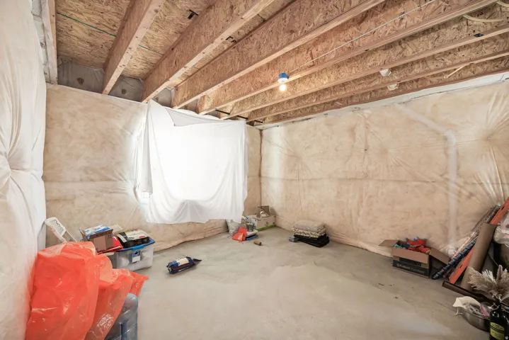 Unfinished basement space with exposed wood joists and subfloor, concrete flooring, and insulated wall surfaces