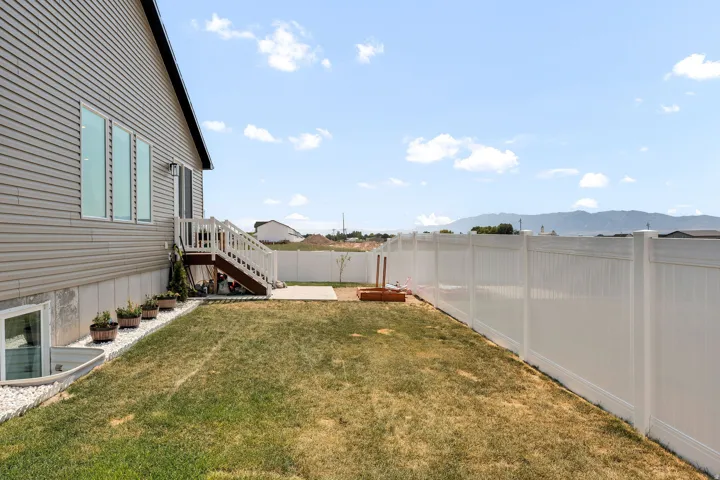 Side exterior featuring a concrete patio, white vinyl fencing, and a terraced lawn