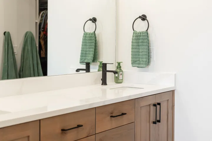 Dual vanity with light wood-finish cabinetry and matte black hardware, white countertop, and wall-mounted mirror
