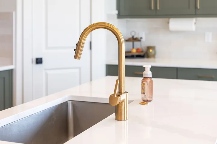 Stainless steel undermount sink with a brass-finish pull-down faucet, set into a white countertop