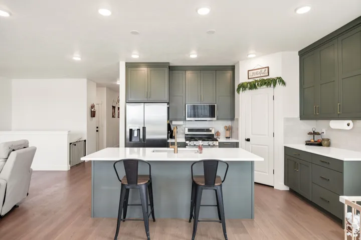 Gourmet kitchen featuring matte green cabinetry, stainless steel appliances, white subway tile backsplash, a large center island with a white countertop, and wood-finish flooring