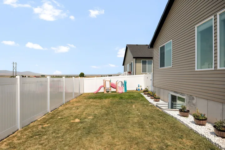 Private backyard with white fencing, a well window, and side yard landscaping featuring white decorative stones