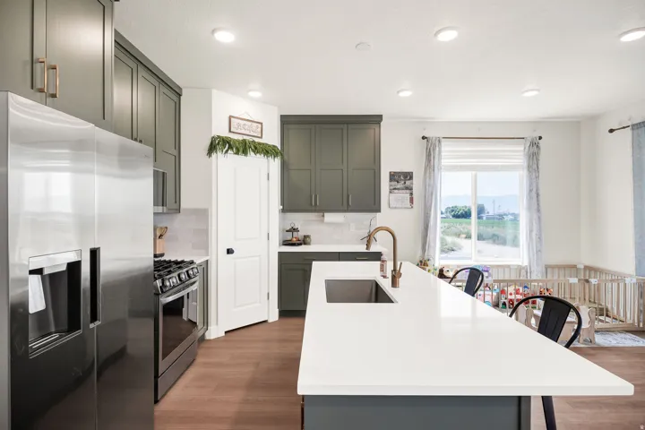 Modern kitchen featuring stainless steel appliances, white subway tile backsplash, quartz waterfall-edge island countertop, soft-close cabinetry in sage and white finishes, wood-finish flooring, recessed lighting, and bronze hardware accents throughout