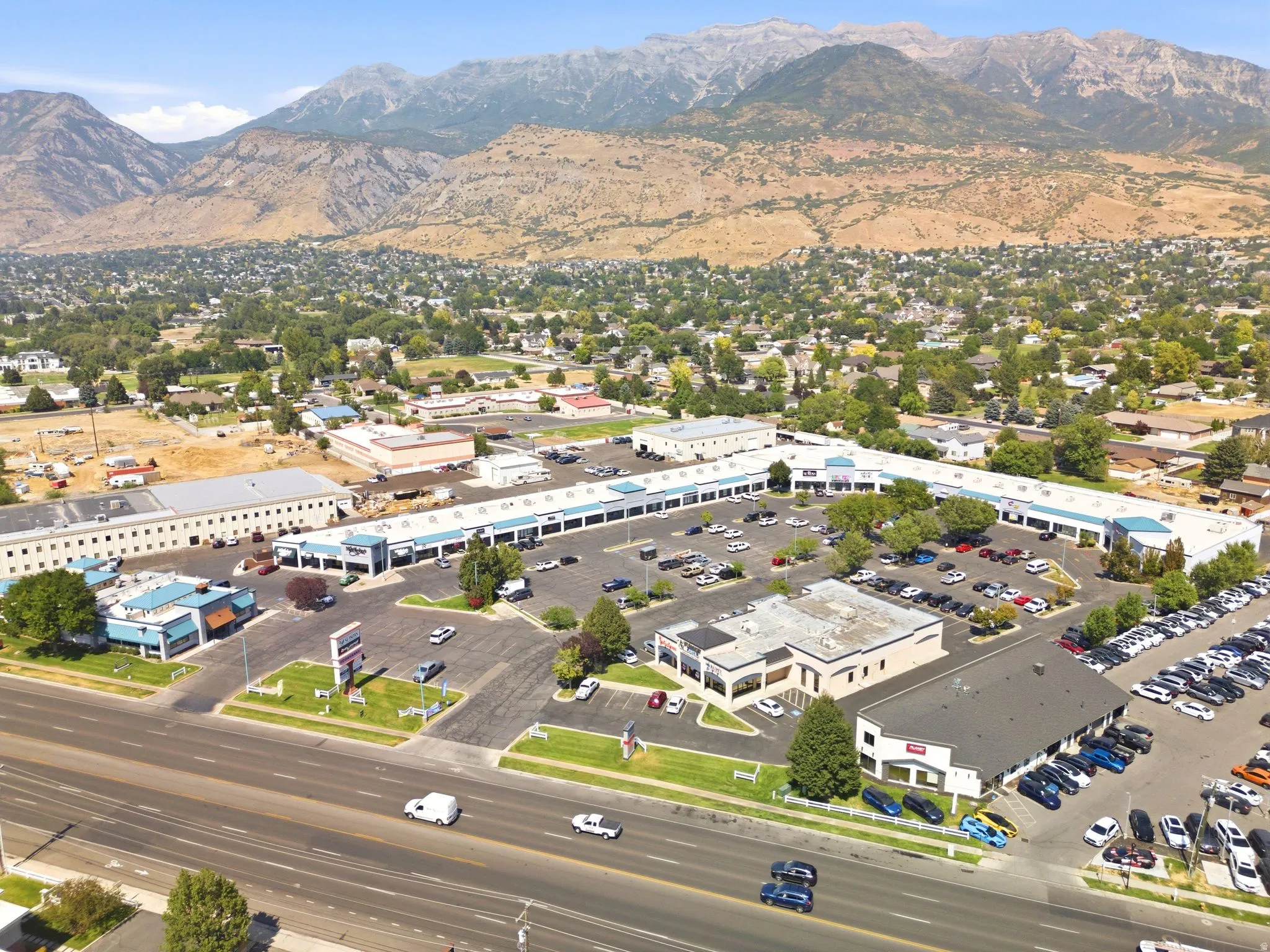 Commercial property featuring multiple retail storefronts, extensive paved parking, direct road frontage, and prominent mountain scenery