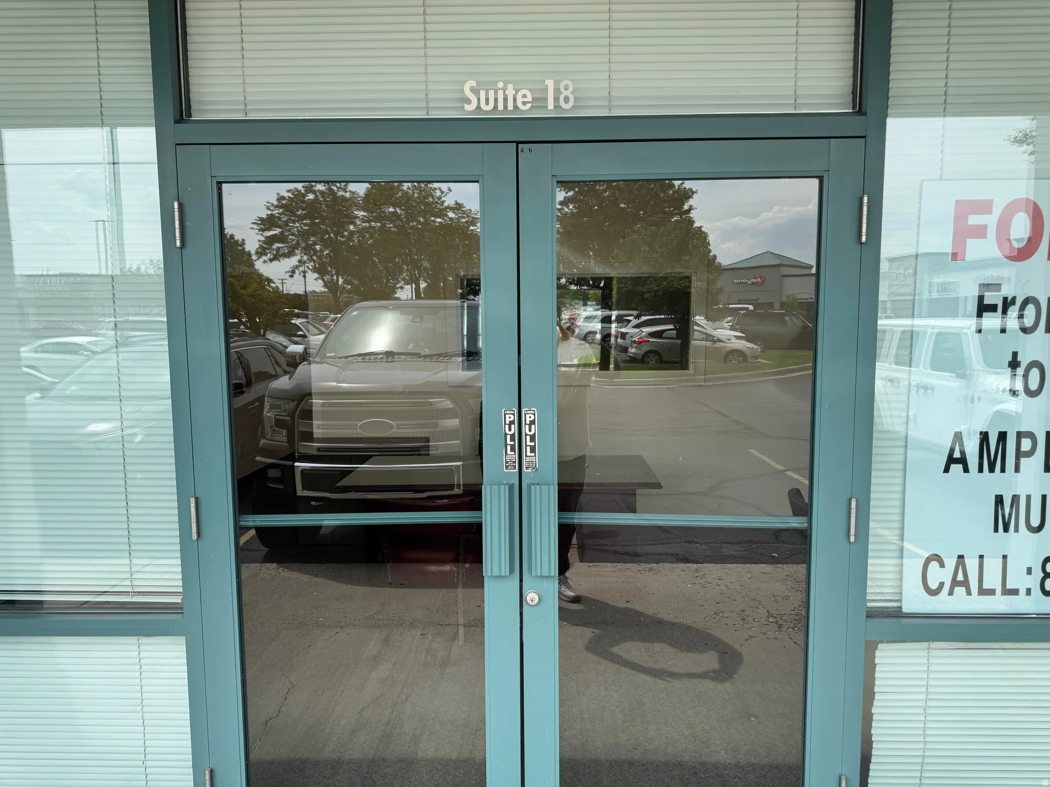 Double glass entry doors with a light blue frame, featuring transom window with horizontal blinds