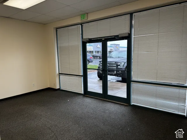 Full-height glass storefront entry with double-door access, floor-to-ceiling windows with integrated blinds, drop ceiling with recessed lighting, and commercial-grade carpeting